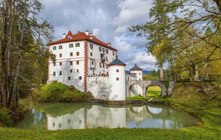 Snežnik Castle reflected in the pond with its bridge and surrounding forest