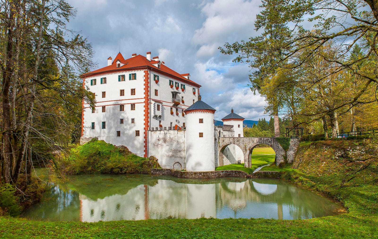 Snežnik Castle reflected in the pond with its bridge and surrounding forest