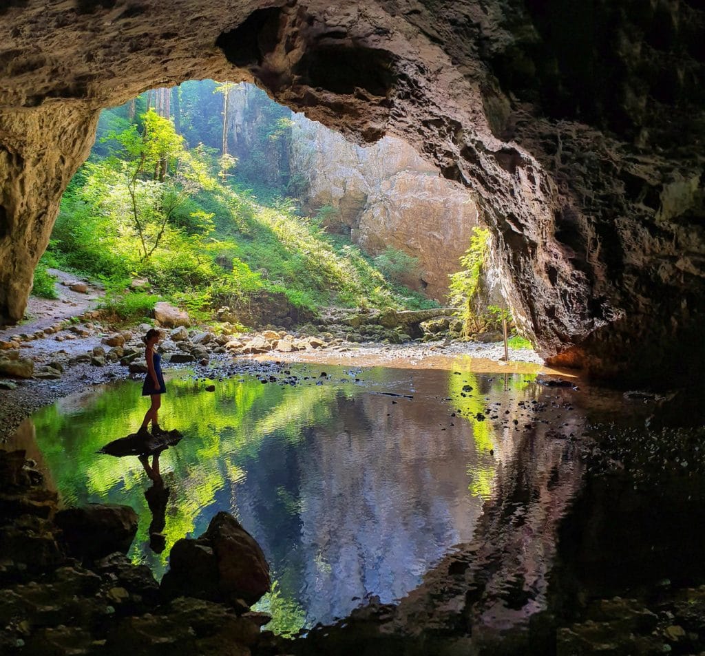 Hiker standing beside the River Rak at a cave opening in Rakov Škocjan