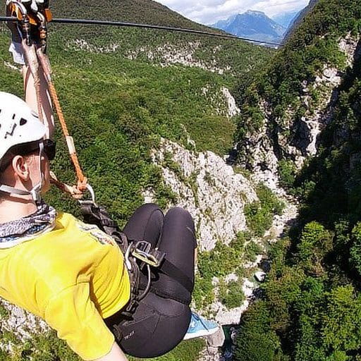 Zipline rider viewed from behind above Učja Canyon with mountains in the distance.