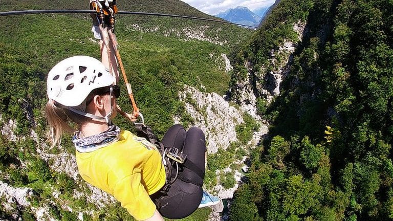 Zipline rider viewed from behind above Učja Canyon with mountains in the distance.