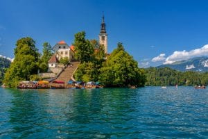 Covered wooden boats are moored below Bled Island’s stone staircase, with the bell tower rising above trees.