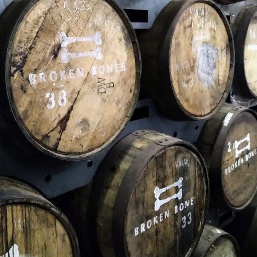 Rows of wooden maturation barrels stacked inside Broken Bones Distillery.