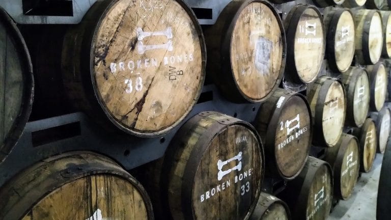 Rows of wooden maturation barrels stacked inside Broken Bones Distillery.