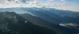 Distant paraglider above dark mountain ridges in the Bohinj valley during evening light.