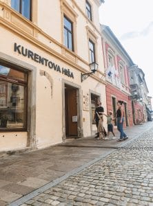 Two adults and two children walk hand in hand near the building's signed entrance on a cobbled street in Ptuj.
