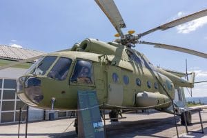 Large green military helicopter displayed outdoors beside an exhibition building in Pivka.