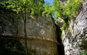 A railed path running along a large limestone wall in Pokljuka Gorge, with a narrow cleft opening to the right.