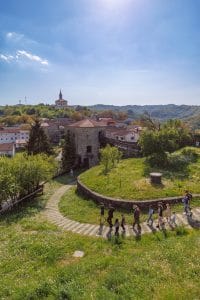 Visitors walking along a path below a round stone tower, with the village of Prem beyond.
