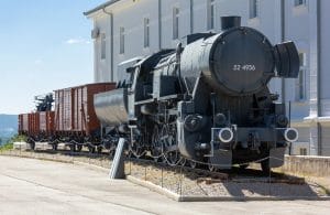 Historic black steam locomotive and freight wagons displayed beside a white museum building in Pivka.