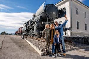 Family taking a selfie beside a large black steam locomotive outside the museum in Pivka.