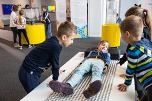Children gather around a child lying on a bed-of-nails exhibit inside Tehnopark Celje.