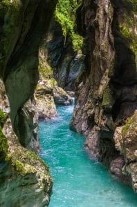 A turquoise river flows through a narrow rock passage with steep, mossy walls.
