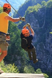 A guide assists a helmeted participant at the zipline departure platform in Učja Canyon.