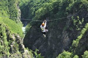 Zipline rider crossing between the steep green walls of Učja Canyon.