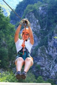 Helmeted rider suspended on a zipline above the forested slopes of Učja Canyon.