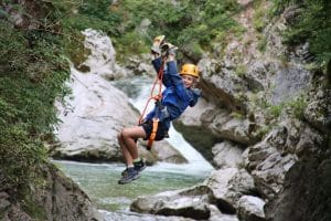 Zipline rider crossing above the river and rocky gorge in Učja Canyon.