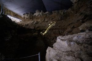 A glowing outline of a perforated bone is projected onto a rough cave wall at Divje Babe.