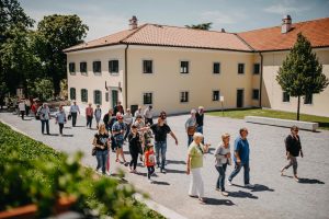 A group of visitors crosses a broad courtyard beside pale historic buildings.